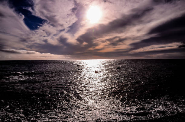 The sun is shining on the ocean, creating a beautiful and peaceful scene. The water is calm and the sky is cloudy, giving the image a serene and tranquil atmosphere