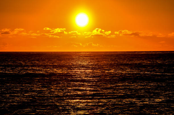 The sun is setting over the ocean, casting a warm glow on the water. The sky is filled with clouds, creating a serene and peaceful atmosphere
