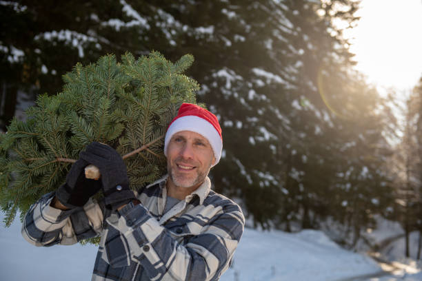 istock Man wearing a Christmas hat carrying a Christmas tree through a snowy forest 2192795116