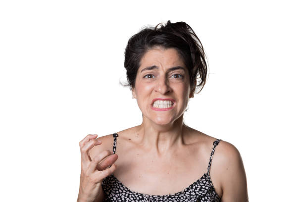An Asian woman in a blue sweater stands against a red background with a playful pout on her face, exuding a mix of light-heartedness and subtle happiness