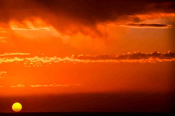 The sun is setting over the ocean, casting a warm orange glow across the sky. The clouds are scattered and the sky is filled with a sense of calmness and serenity
