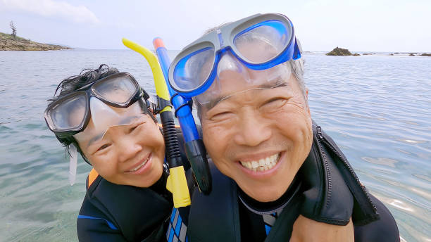 asian elderly couple is snorkeling and smiling cheerful happy taking a selfie smiling at the camera- they have courage to try new things with personality unrestricted