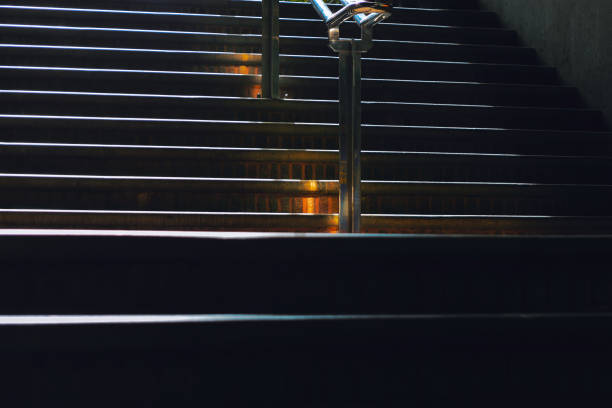 Stairs with metal railings are partially illuminated by light from above, creating an intriguing interplay of shadow and light. Contrast enhance structure of stairs emphasizing architectural details