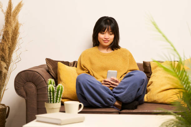 Young asian woman using smartphone on sofa at home