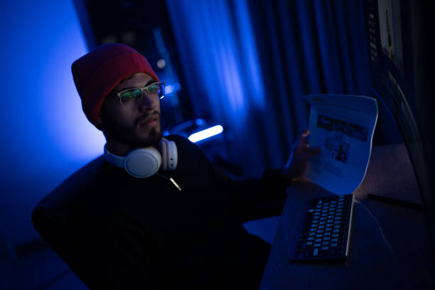 istock Young man wearing headphones works at a computer in a dimly lit room with blue lighting at night 2192808028