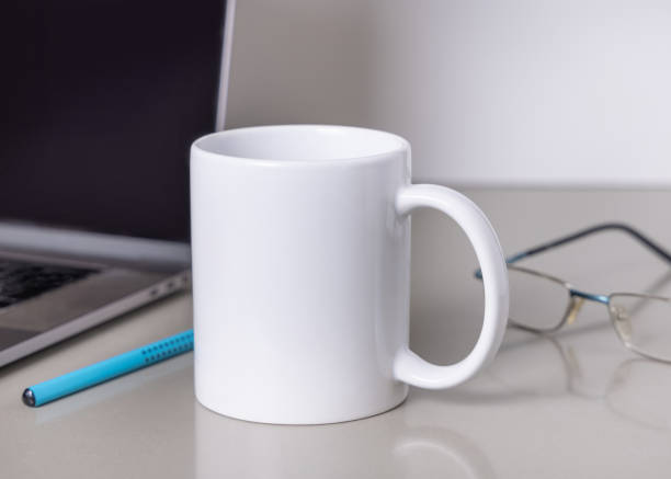 istock White coffee mug on grey office table against laptop, glasses and pencil closeup, mockup 2192808363