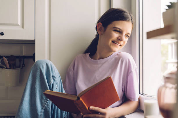 istock Reflective girl gazes outside by window with book 2192819753