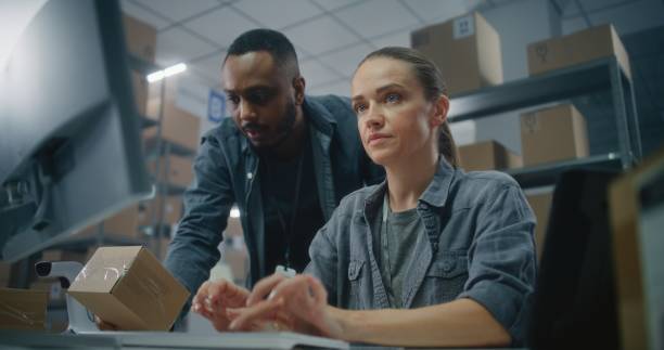 istock African American warehouse employee scans code on parcel. Female logistics specialist uses computer 2192825018