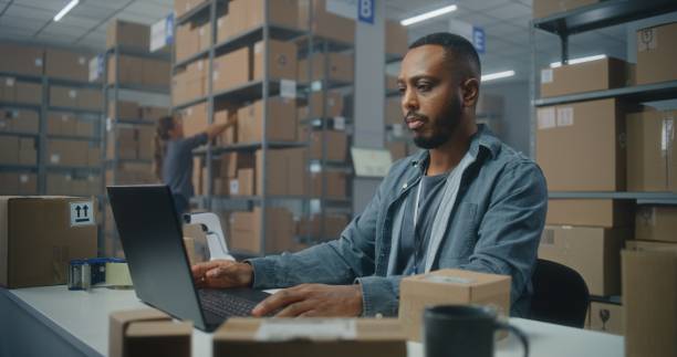 istock Postal service: African American logistics specialist scans parcel, uses laptop computer 2192825199