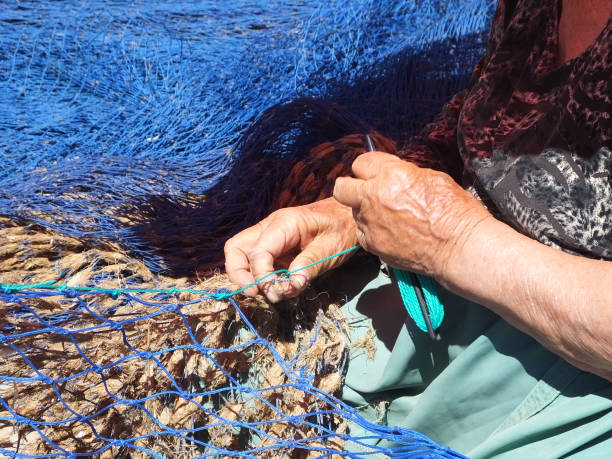 Skilled lady repairing fishing nets by hand.