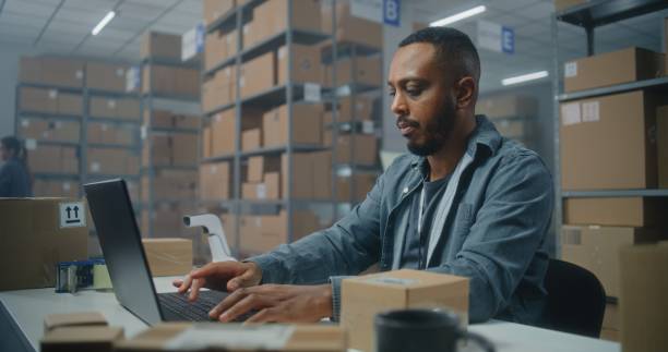 istock African American warehouse clerk scans parcel with barcode scanner, uses laptop 2192827305