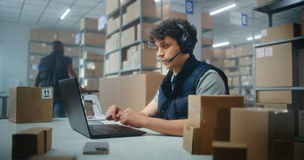 istock Customer support specialist in logistics wearing headset talks to customer on call, uses laptop 2192828957