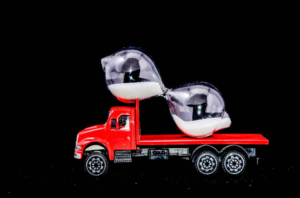 A red truck is carrying two sandglasses. The truck is on a black background. The sandglasses are shaped like hourglasses