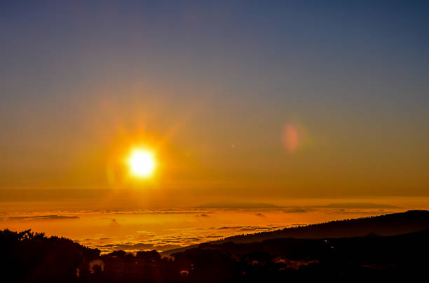 The sun is setting over a mountain range, casting a warm glow over the landscape. The sky is a deep blue, with a few clouds scattered throughout. The scene is peaceful and serene