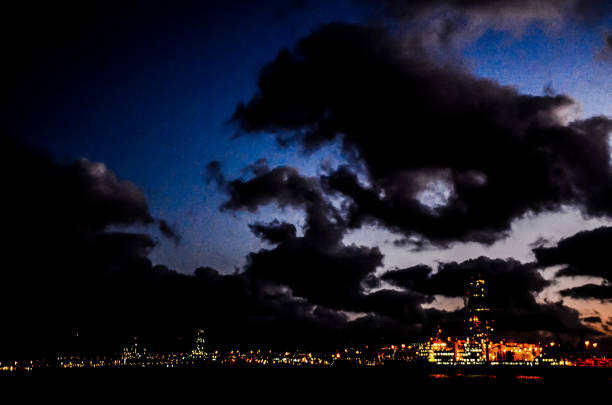A dark sky with clouds and a city in the background. The city is lit up at night