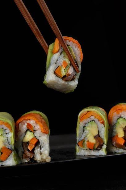 istock Vegetable sushi roll being held by wooden chopsticks against a black background. 2192833485