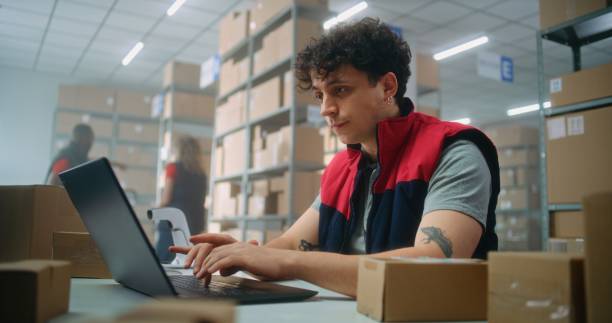 istock Parcel processing specialist scans package, prepares for shipping to customer, works on laptop 2192833487