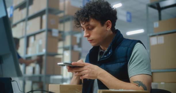 istock Logistics manager scans small parcels using smartphone, works in warehouse of post office 2192836421