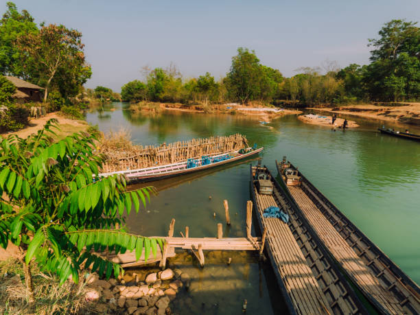 Peaceful view of small river with wooden boats, surrounded by lush greenery and serene landscapes. A depiction of traditional life and nature in a rural area of Myanmar.