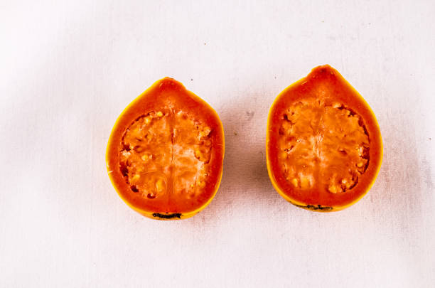 Two pieces of fruit, one of which is a tomato, are cut in half and placed on a white background