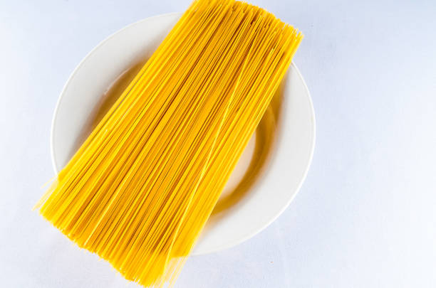 A plate of yellow pasta is on a white plate. The pasta is long and thin, and it is sitting on top of the plate