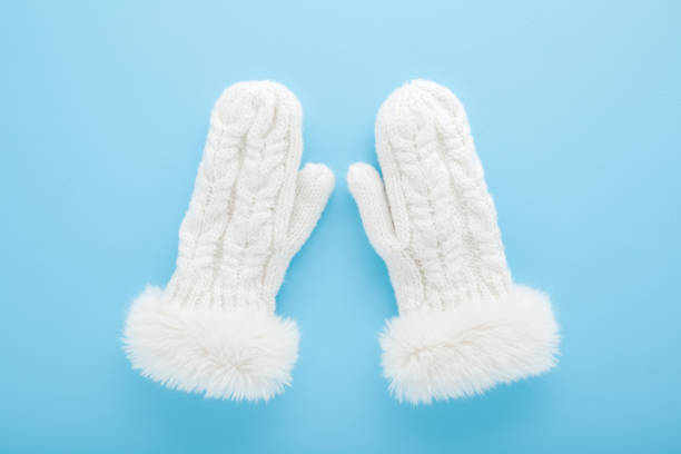 White soft knitted warm winter female mittens with fluffy fur on light blue table background. Pastel color. Closeup. Top down view.