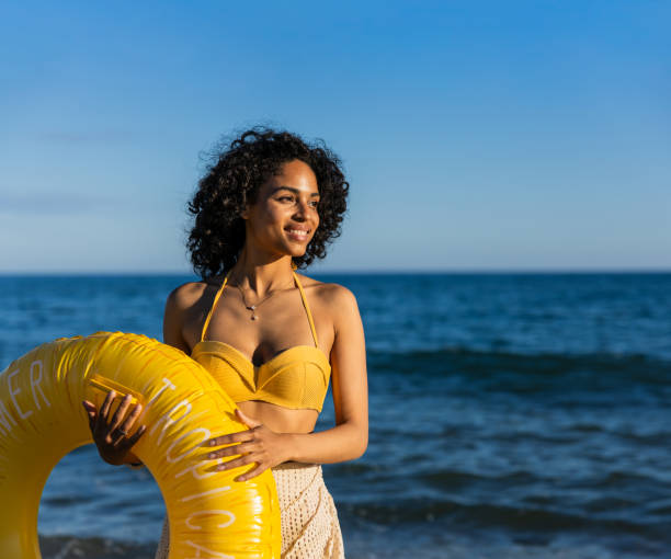istock Young latin woman holding inflatable ring at beach 2192842086