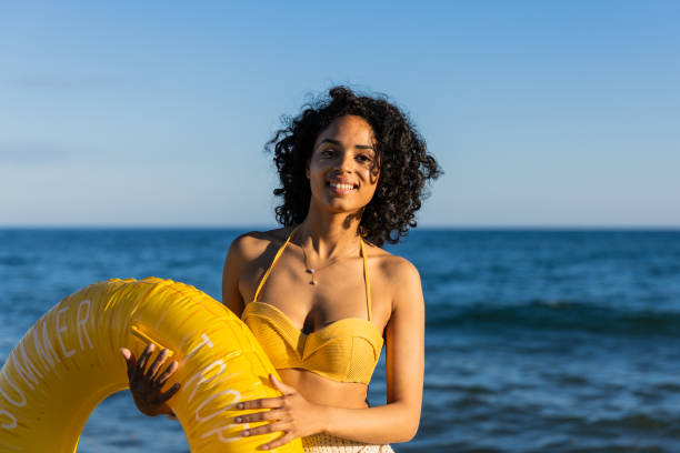 istock Young latin woman smiling and holding inflatable ring at beach 2192842113