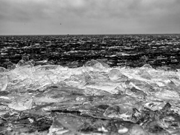 Monochrome image of a frozen sea with jagged ice formations under a cloudy sky, creating a stark and dramatic scene.