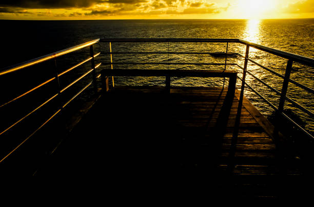 A wooden pier with a railing overlooking the ocean. The railing is dark and the water is calm