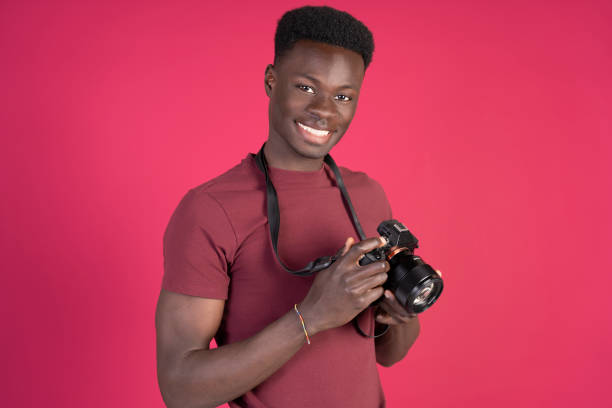 istock Young photographer smiling and holding a camera on pink background 2192870984