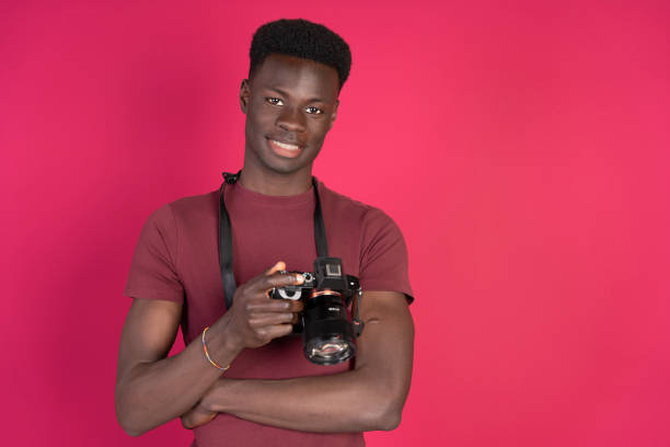 istock Young photographer smiling and holding a camera on pink background 2192871145