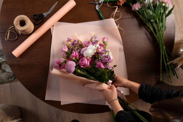 istock Collecting bouquet from carnations and roses, top view. Florist making a bouquet composition from flowers on the wooden table background. 2192871491