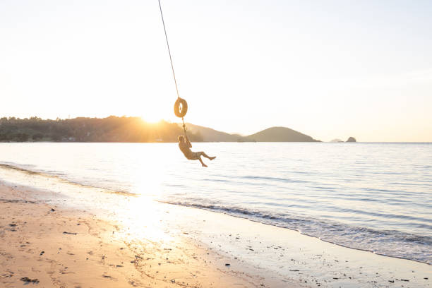 Tourist woman relaxing on a swing and enjoying the ocean view while vacationing at a tropical beach resort during her holiday
