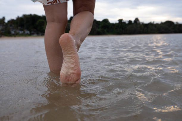 Barefoot person wading through shallow beach water. Tranquil scene of leisure and calm.