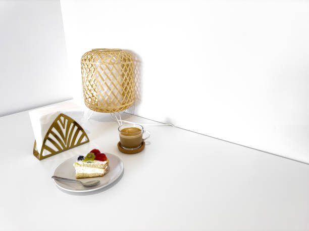 Cozy minimalist dessert setup with cake, coffee, and lamp on white table.