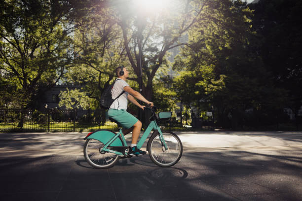 Urban cyclist riding a teal bicycle in a sunny park, surrounded by trees and enjoying nature. The setting creates a peaceful and refreshing atmosphere for outdoor activities and commuting.