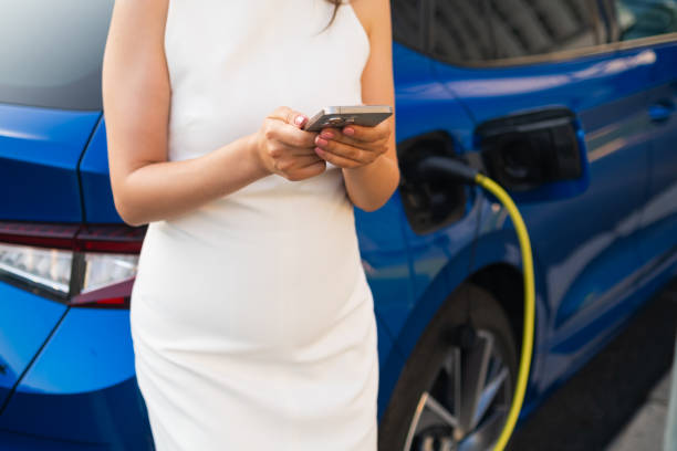istock Woman charging a blue electric car while using smartphone in a sunny day. 2192898138