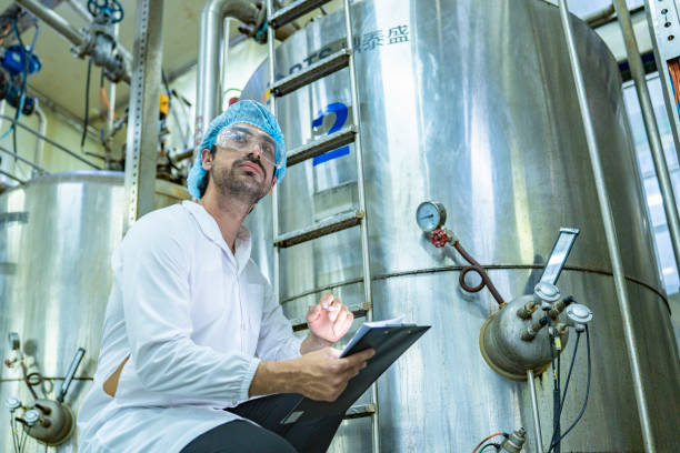 istock Worker examining an industrial tank and recording data on a clipboard, emphasizing the importance of safety, quality assurance, and technological advancement in industrial environments. 2192901466