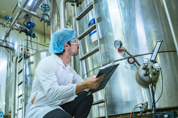 istock Worker examining an industrial tank and recording data on a clipboard, emphasizing the importance of safety, quality assurance, and technological advancement in industrial environments. 2192902039