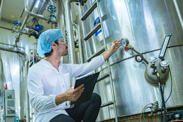 istock Worker examining an industrial tank and recording data on a clipboard, emphasizing the importance of safety, quality assurance, and technological advancement in industrial environments. 2192902420