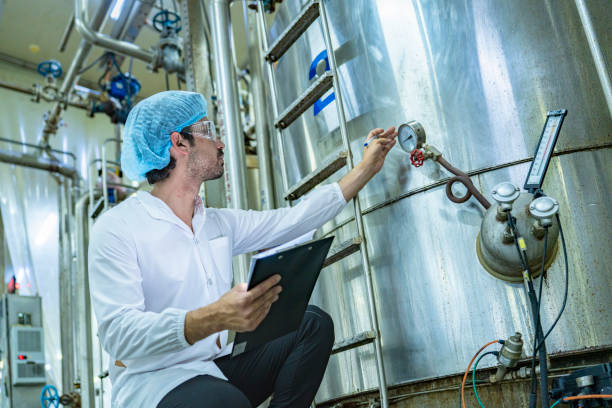 istock Technician in protective gear evaluating a production tank, representing quality assurance, meticulous processes, and expertise in industrial manufacturing. 2192902550