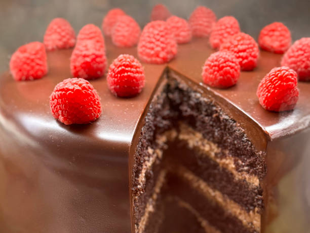 Stock photo decadent chocolate raspberry gateau, freshly sliced, showcases its rich layers of chocolate cake paired with tangy raspberry filling. Topped with smooth butter icing and creamy frosting, it exudes bakery-fresh charm
