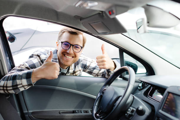 istock Young man looking through window inside new car, checking it before purchase at modern dealership store. Cheerful guy buying or renting automobile at showroom 2192908212