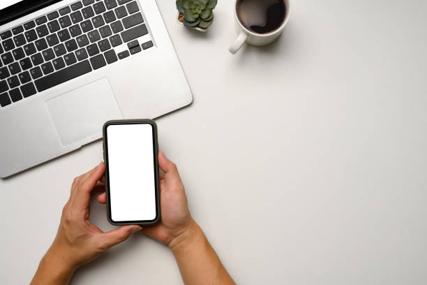 istock Above view of hands holding a smartphone with blank screen on white desk 2192911020