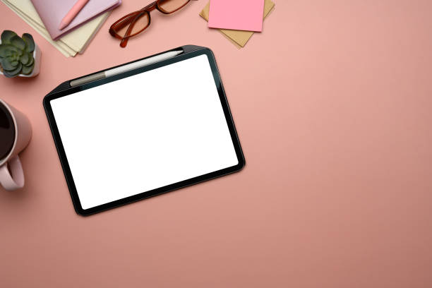 istock Digital tablet with a blank screen, glasses, coffee mug and notebooks on a soft pink background 2192911030