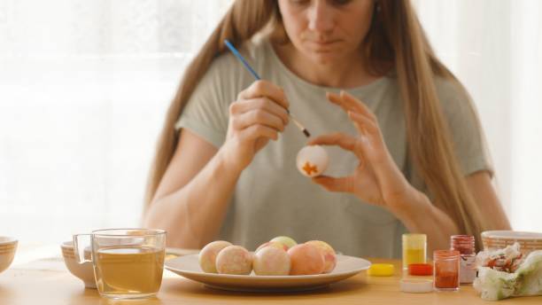 istock A Woman Paints an Orange Flower on a White Egg While Concentrating Intently. 2192919742