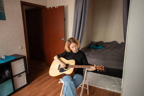 istock music lessons, Woman learning guitar, playing indoors, building musical skill, studying classic guitar techniques 2192920521