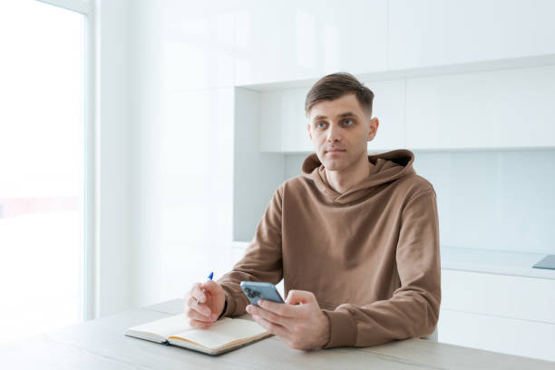 istock Man is sitting at a table with a cell phone in his hand and a pen on the table 2192923363