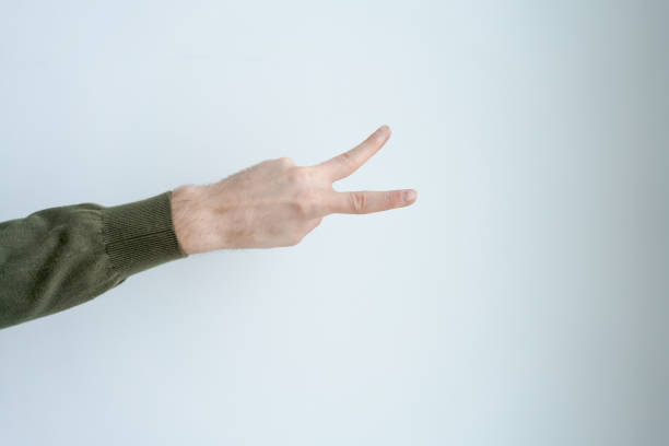 Hand is pointing to the sky with two fingers. The hand is wearing a green sweater. Concept of peace and tranquility